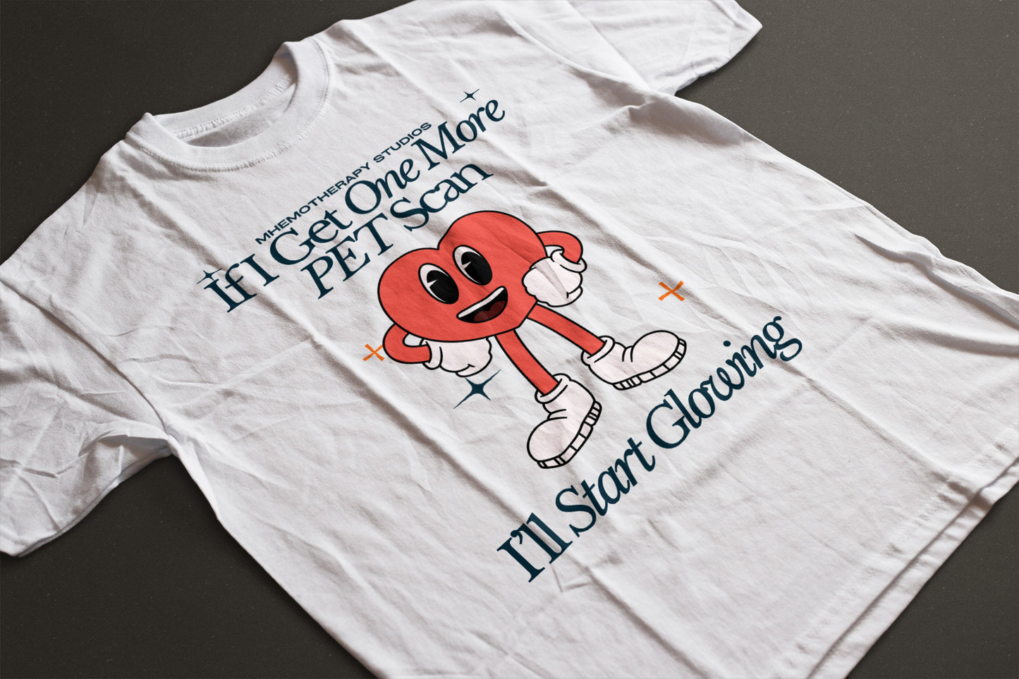 Flat lay view of the white "If I Get One More PET Scan, I'll Start Glowing" funny cancer survivor t-shirt for women and men by Mhemotherapy.com.